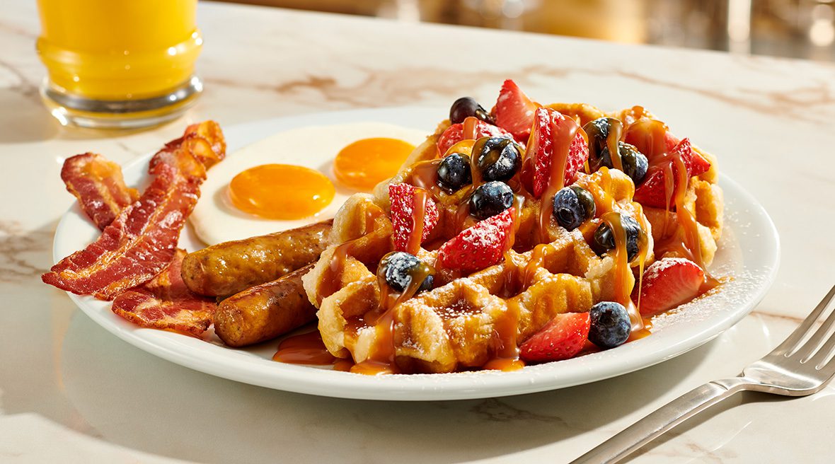 A plate of food with waffles, eggs and fruit.